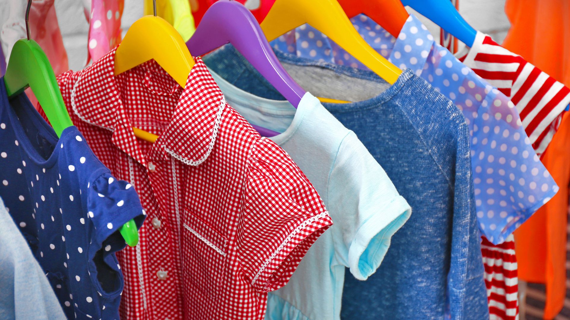 auf bunten Plastikbügeln hängen hintereinander verschiedenfarbige kurzärmelige Kinderhemden.